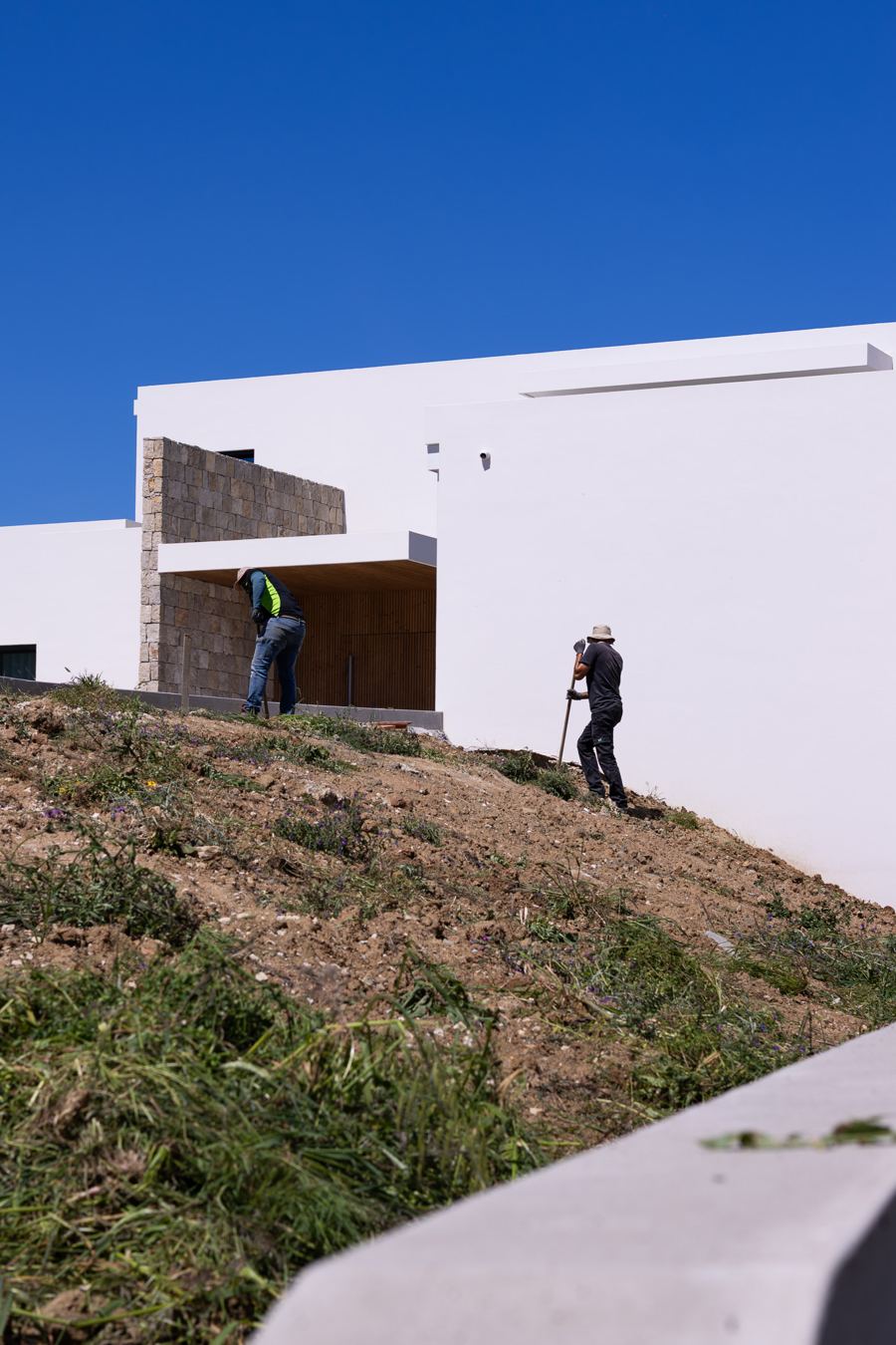 Equipa a trabalhar no talude junto a uma moradia branca